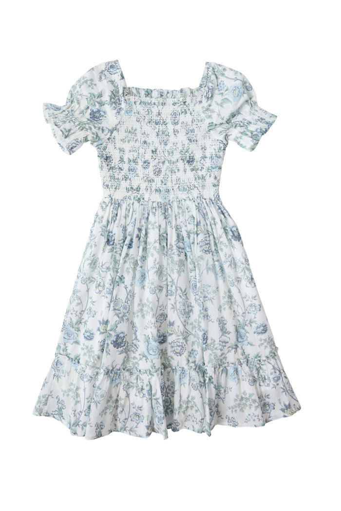 The Mini Valencia Dress in Ivory Climbing Vine Bloom by Ivy City Co is a charming girls’ smocked dress, featuring short puff sleeves, a blue floral pattern on white fabric, a smocked bodice, square neckline, and a ruffled hem.