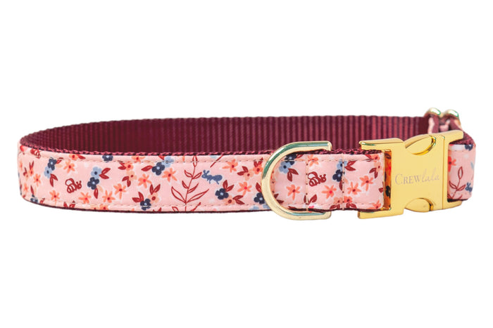 Stylish dog collar featuring a pink floral print with bees and leafy accents in warm and cool tones, reinforced with nylon webbing, and finished with polished metal hardware including a D-ring and clasp closure.