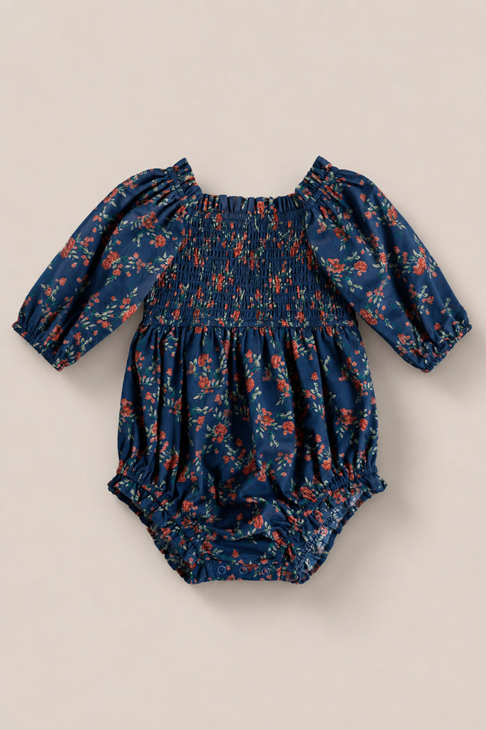 The Ivy City Co Baby Madeline Romper in Midnight Vibrant Chintz features a smocked bodice, red and orange floral print, elastic cuffs and leg openings, shown on a plain beige background.