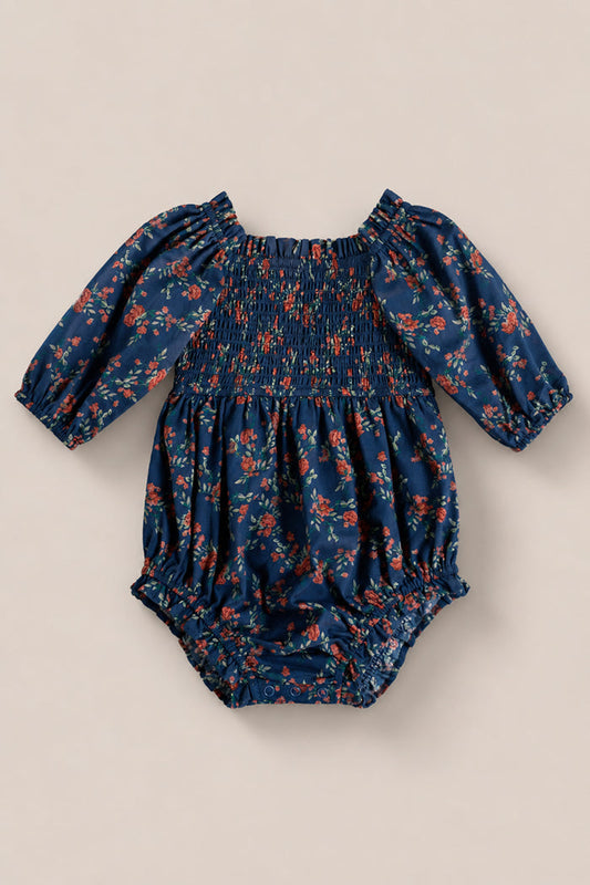 The Ivy City Co Baby Madeline Romper in Midnight Vibrant Chintz features a smocked bodice, red and orange floral print, elastic cuffs and leg openings, shown on a plain beige background.