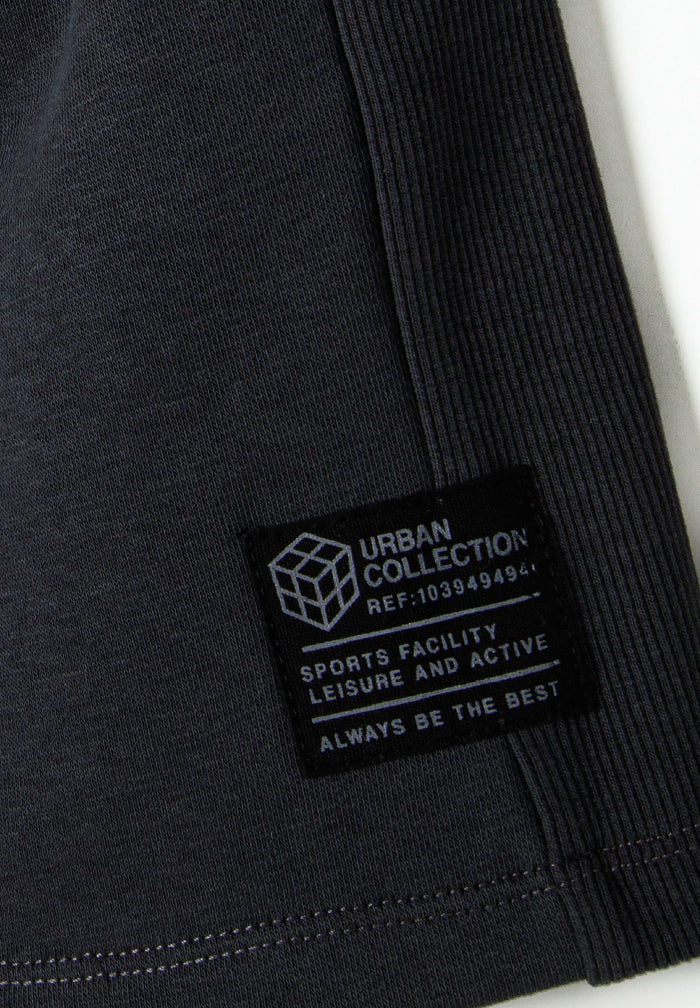 Detail of boys fleece shorts featuring ribbed fabric panels and a decorative patch.