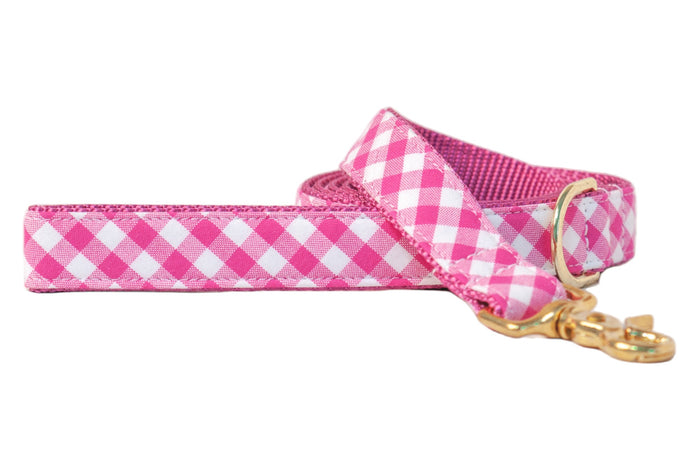 Fuchsia and white plaid dog leash with a classic checkered fabric exterior and sturdy webbed interior. Features a gold-tone metal clasp and D-ring for secure attachment and added style.