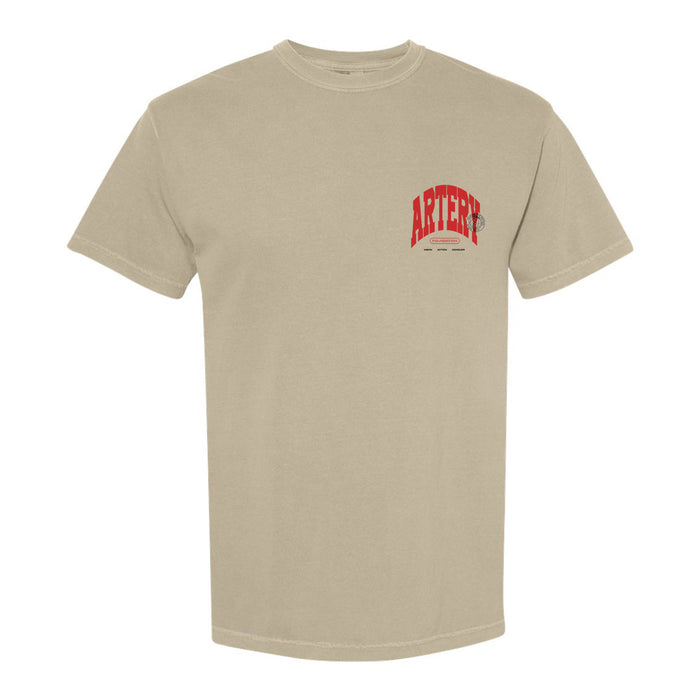 A plain beige Artery Foundation Comfort Colors T-shirt with "ARTERY" in large red letters and a small black graphic and text on the left chest, crafted from soft ring-spun cotton.