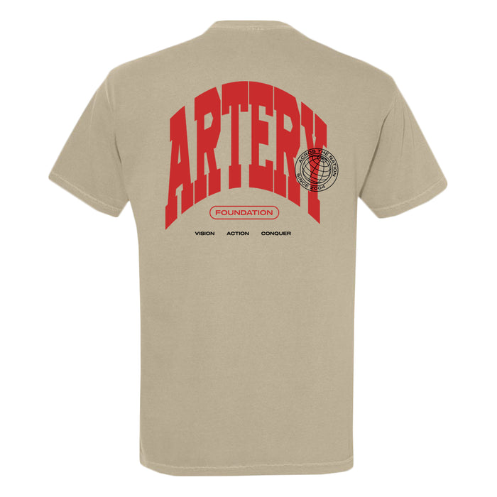 The Artery Foundation beige Comfort Colors T-shirt features bold red ARTERY text, a red FOUNDATION oval and globe graphic, plus “VISION, ACTION, CONQUER” in black on the back, all on garment-dyed, ring-spun cotton.