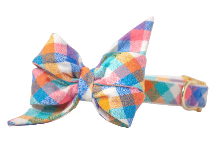 A vibrant dog collar with an oversized feminine belle bow in multicolor pastel plaid — featuring cheerful shades of pink, blue, orange, and teal with polished hardware.