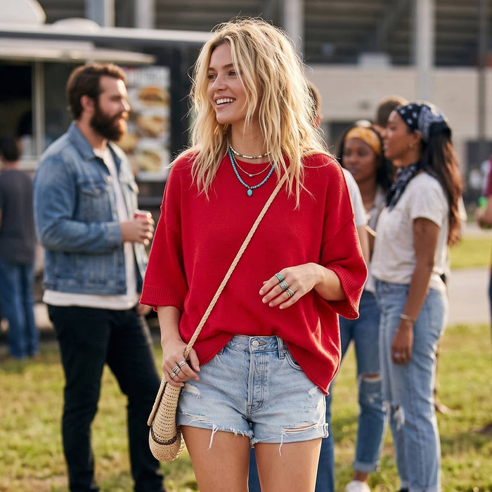 Woman in a red sweater and denim shorts walking outdoors with people in the background