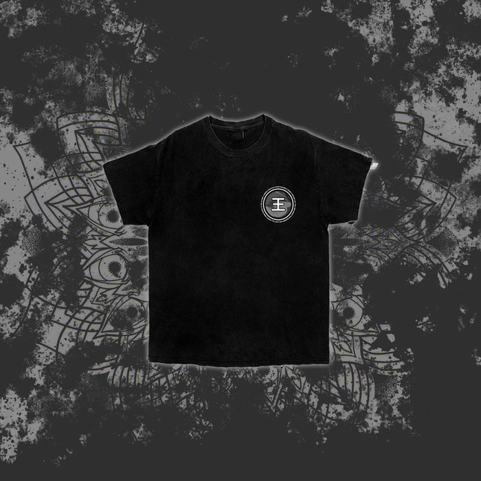 A black Reflections t-shirt with a white circular emblem on the left chest is centered on a dark, splattered background featuring a faint decorative mandala pattern.