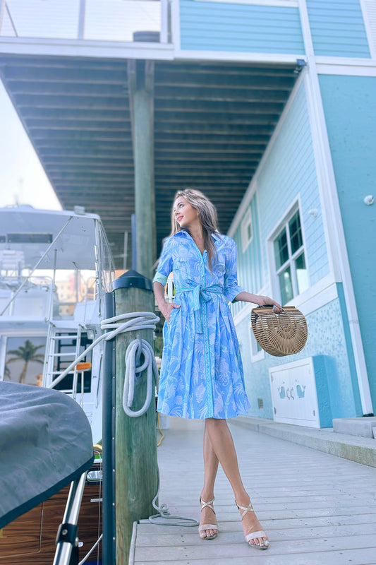 Model in a knee length blue, green, and white patterned dress with a green patterned contrast on the cuff.