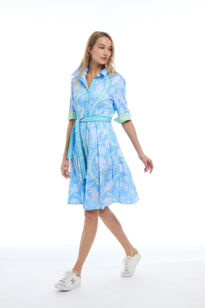 Model In green, blue, and white floral pattern knee length dress. Collar, green patterned contrast sleeves, and belt tie