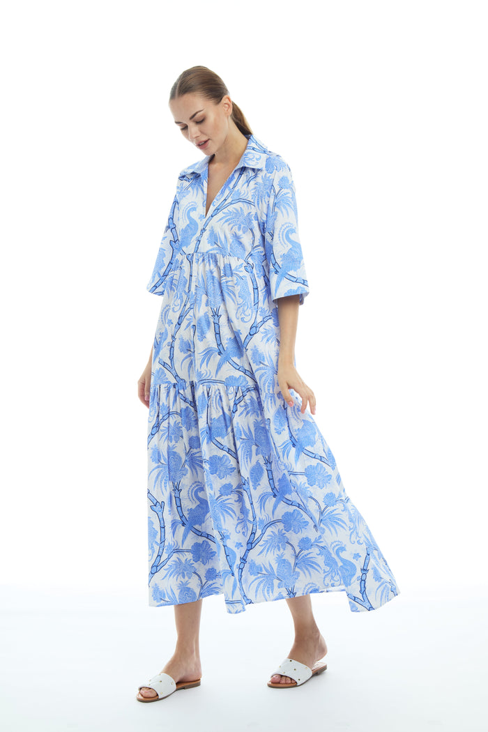 Model in a tiered midi length dress, with a white background and blue peacocks and floral pattern