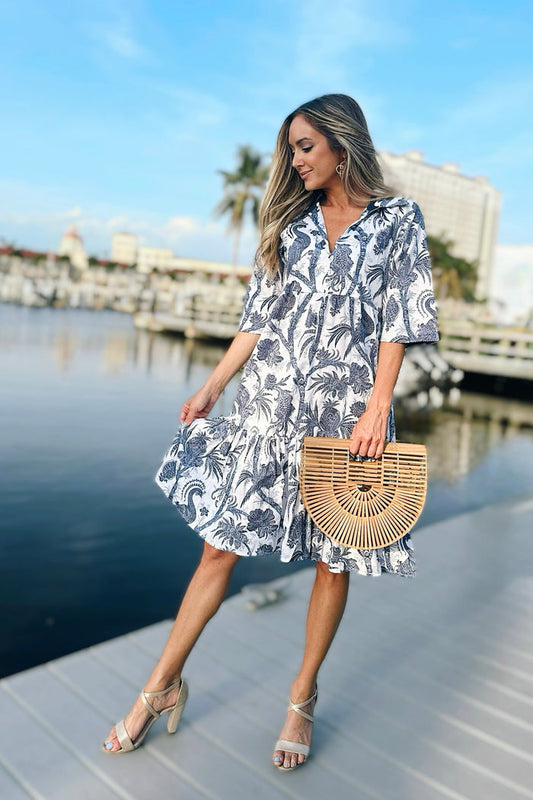 Model on a dock wearing a short sleeve navy and white floral print dress. A line with a ruffle at the bottom