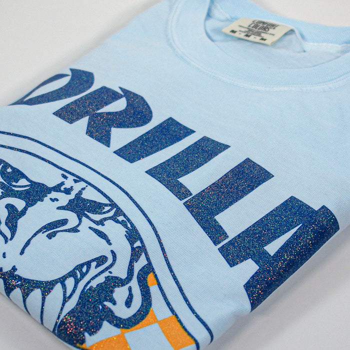 A light blue garment-dyed cotton folded t-shirt by Gorilla Biscuits featuring a bold, glittery gorilla face graphic and “GORILLA” in large blue letters on the front.