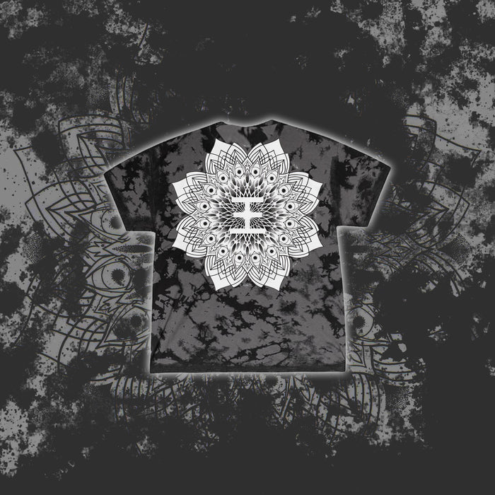 A black and gray tie-dye Reflections T-shirt features a bold white mandala design centered on the chest, set against a matching mandala and splatter background—ideal for fans of printed tees.