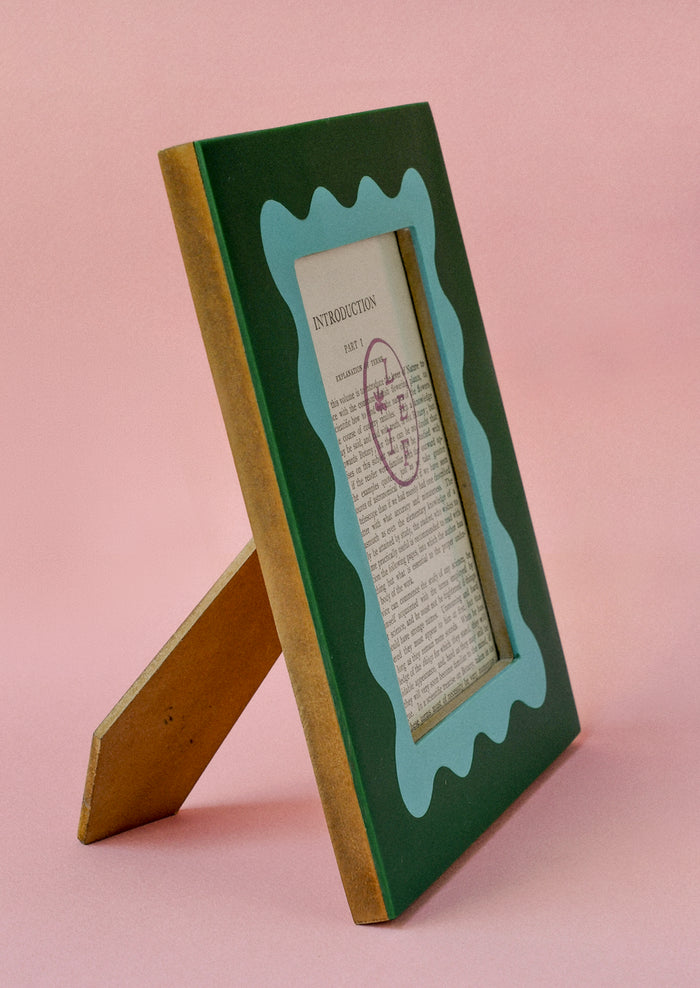 Side view of a green picture frame with an aqua squiggle frame around picture opening.
